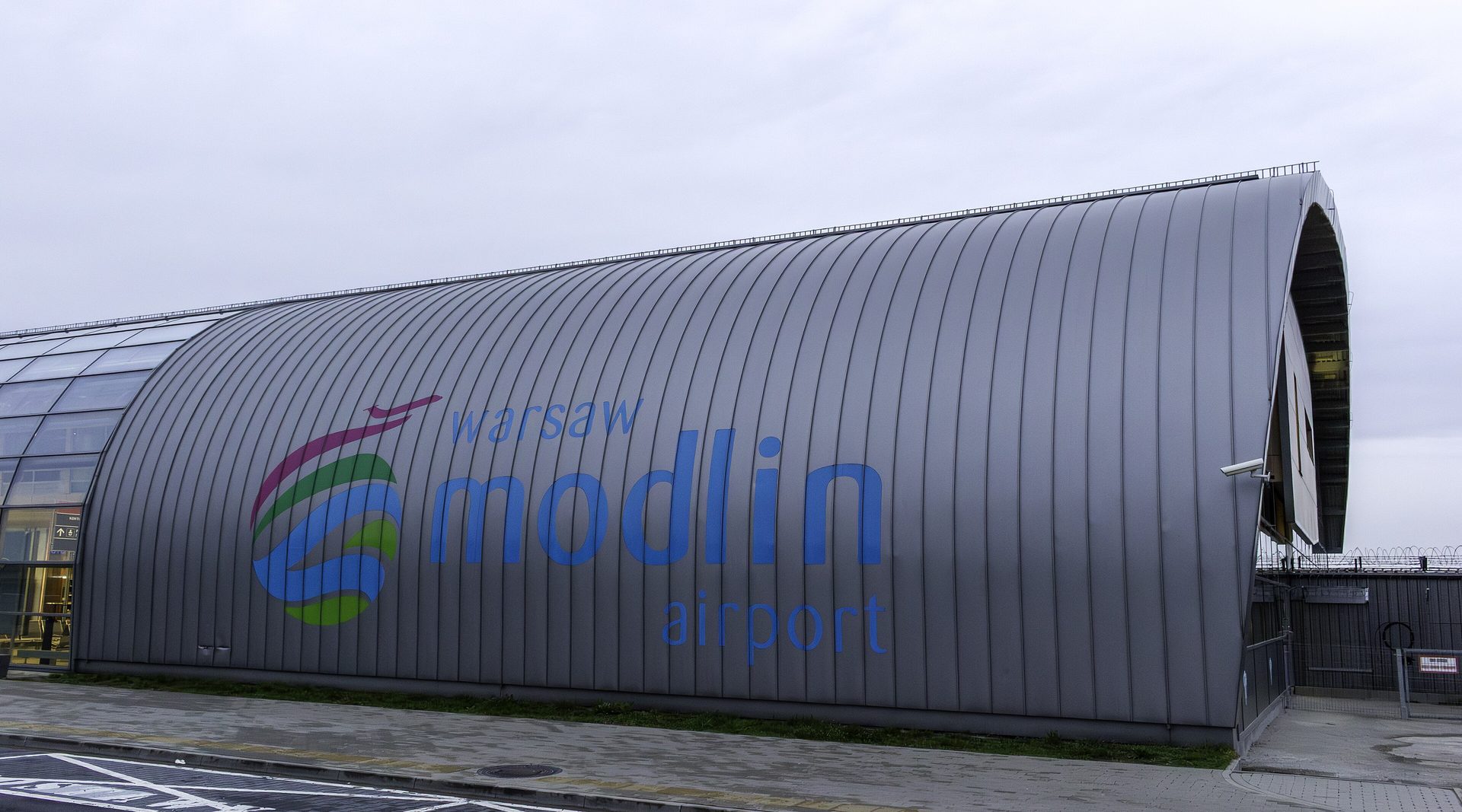 The curved silver shell of the Warsaw Modlin Airport terminal, carrying the airport's name across its side